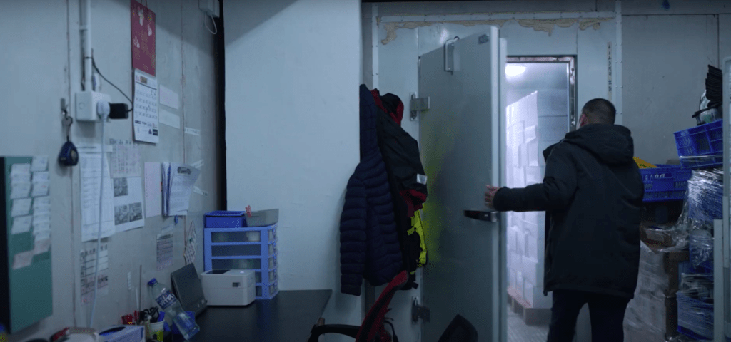 A man is positioned in an SME office, looking towards a door, with simple furnishings and warm lighting.